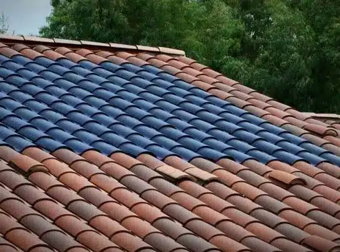 Toit avec section de tuiles solaires bleues intégrées parmi les tuiles traditionnelles terracotta.